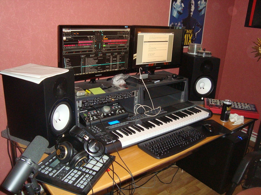 A young musician wearing headphones and working on a laptop in a home studio setting.